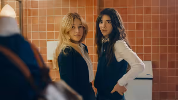 Two students in dark uniforms turn toward someone in a tiled school bathroom