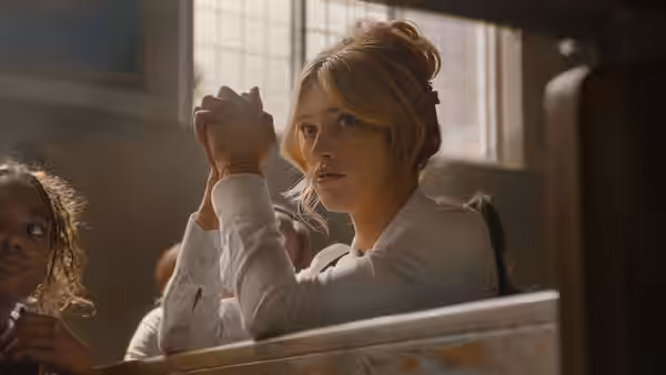 A young woman clasps her hands in a wooden pew beside another girl