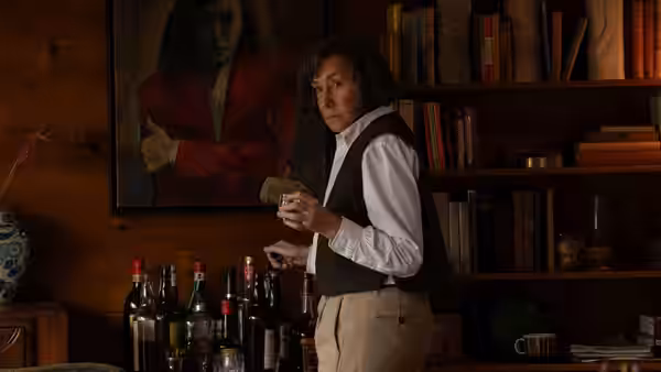 Patricia Highsmith (Helen Mirren) stands in a wood-paneled library, holding a drink