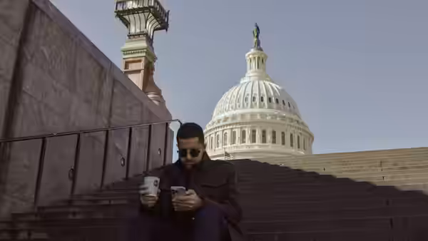 A man seated on the steps of the Capitol building checking his smartphone