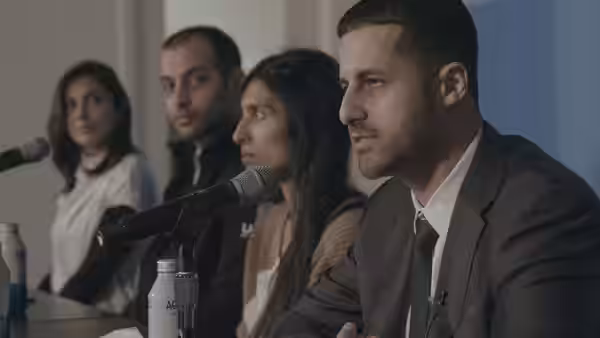 A panel of speakers at a press conference table with microphones and water bottles
