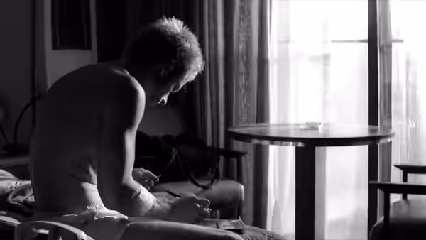 Leonard (Guy Pearce) sits on a bed examining marks on his hands