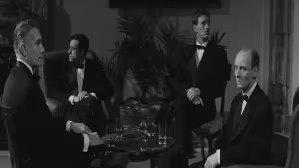 Men in tuxedos sit around a table in an elegant hotel room