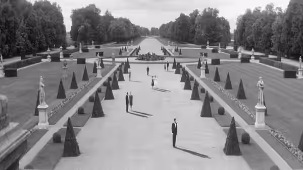 Figures stand far apart along a formal garden's symmetrical paths and rows of trees
