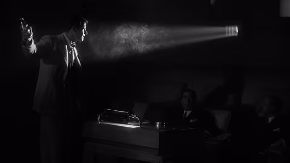 Man in suit gestures with raised arm beside desk with typewriter