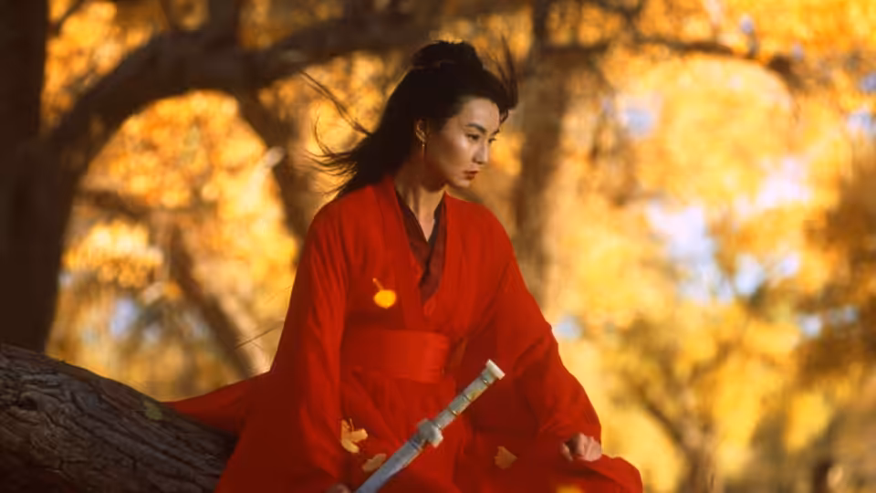 Flying Snow (Maggie Cheung) seated on a tree branch holding her sword