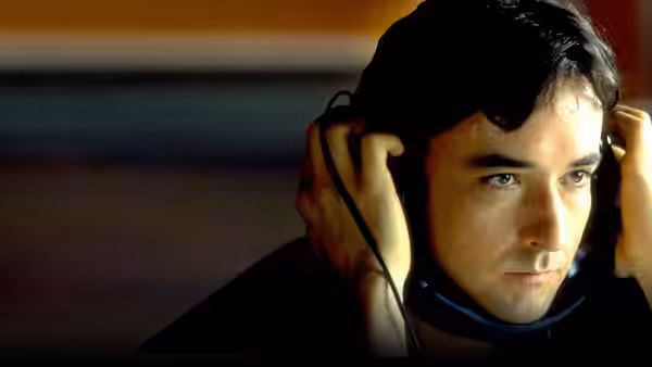 Rob (John Cusack) listening closely with headphones over his ears