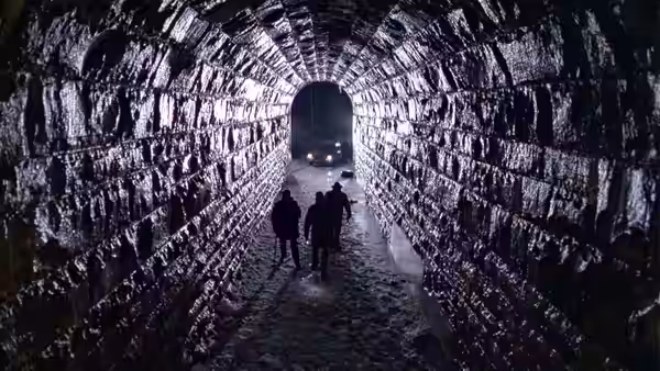 a group of people walking through a rocky tunnel illuminated by distant lights
