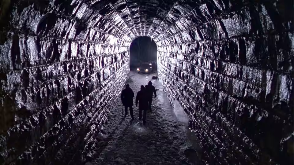 a group of people walking through a rocky tunnel illuminated by distant lights
