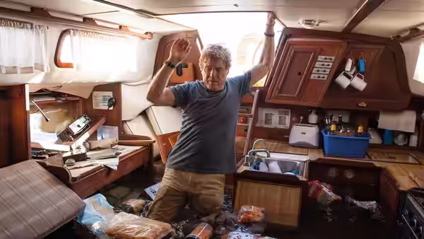 Our Man (Robert Redford) stands amid scattered supplies inside the sailboat cabin
