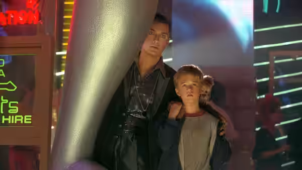 Gigolo Joe (Jude Law) stands with David (Haley Joel Osment) amid neon lights at night