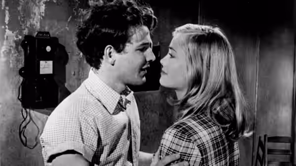 Young man and woman stand face to face in close conversation indoors