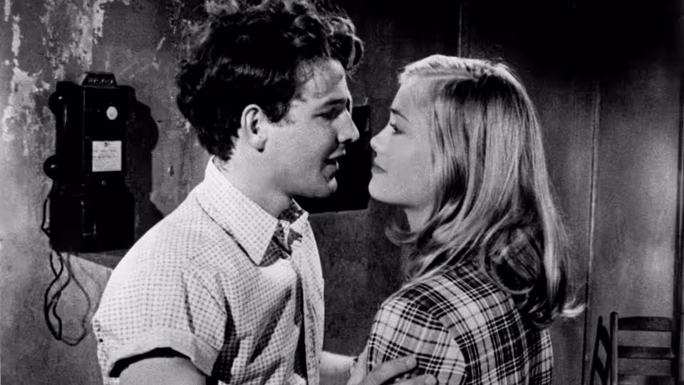 Young man and woman stand face to face in close conversation indoors