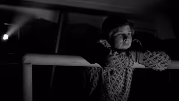 Billy (Sam Bottoms) leans on a railing at night wearing a cap