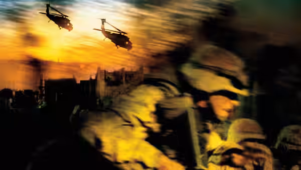 Soldiers advancing at dusk with helicopters overhead in a smoky sky