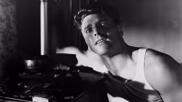 'Swede' Andersen (Burt Lancaster) leans beside a typewriter, looking upward