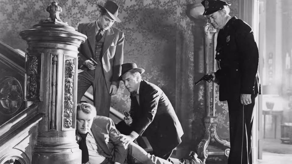 Several men search around an open safe as a uniformed police officer watches