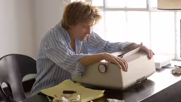 Karen Eiffel (Emma Thompson) leaning over a typewriter on a desk