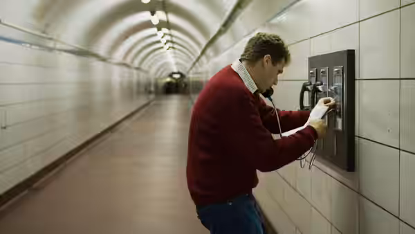 Harold Crick (Will Ferrell) operating a payphone in a tiled subway corridor