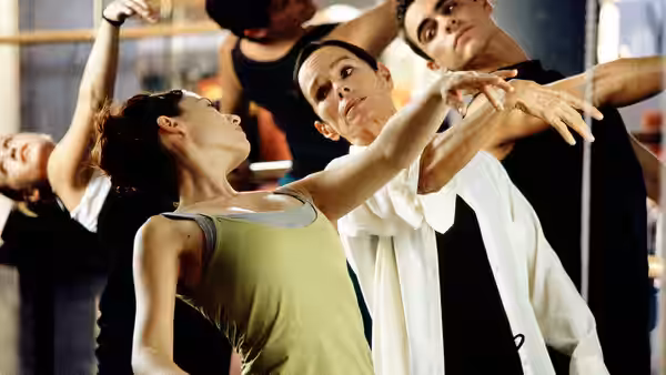 Dancers in a studio holding extended arm poses during rehearsal