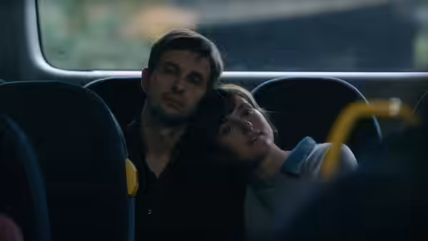 A woman rests her head on a man's shoulder on a bus
