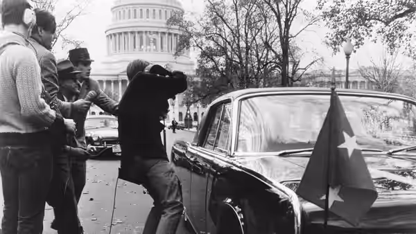 Men gather beside a car flying a flag near the Capitol
