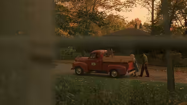 Two men stand beside a red pickup truck parked outside a house
