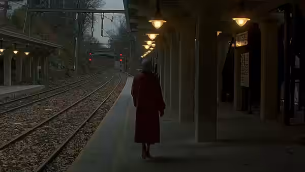 A person in a red coat walks alone along an empty train platform