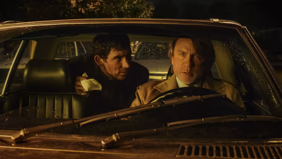 Benoit Blanc (Daniel Craig) driving at night with Fr. Jud Duplenticy (Josh O'Connor)