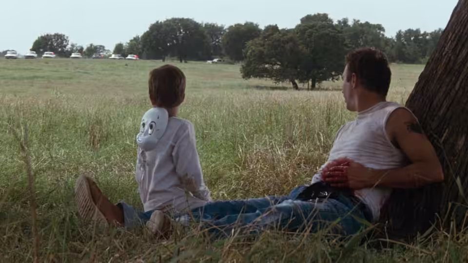 Butch Haynes and Phillip sit beneath a tree overlooking a grassy field