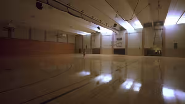 An empty school gymnasium with a polished wooden floor and one person in the distance
