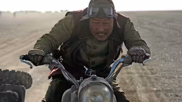 Yoon Tae-goo (Song Kang-ho) grips the handlebars of a motorcycle in the open desert