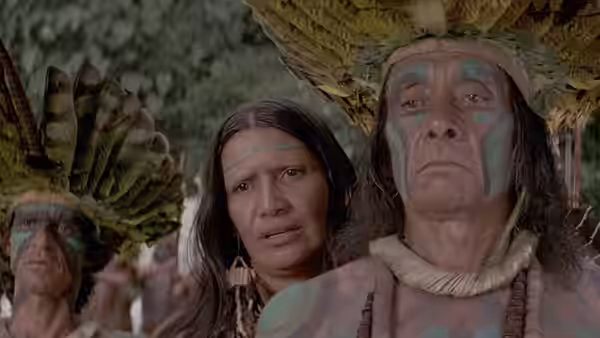 A painted Indigenous man and woman stand beneath a feathered headdress