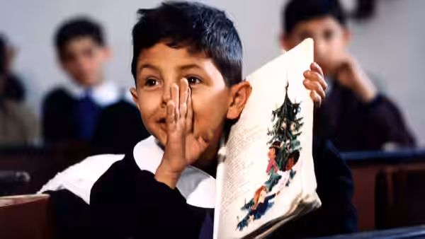 Young Totò sitting in class with an open book in his hand