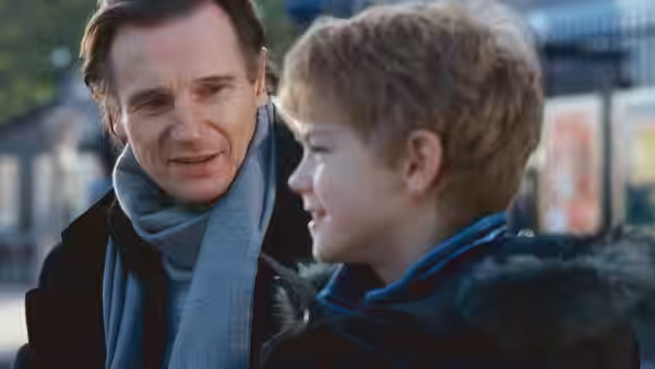 Daniel (Liam Neeson) talking with a young boy outdoors during the day