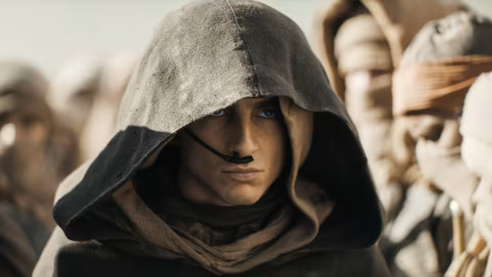 Paul Atreides (Timothée Chalamet) standing among hooded Fremen in the desert