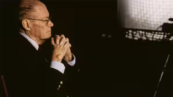Robert McNamara in profile with hands clasped near his face