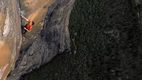 Alex Honnold climbing a steep rock face with dense forest below