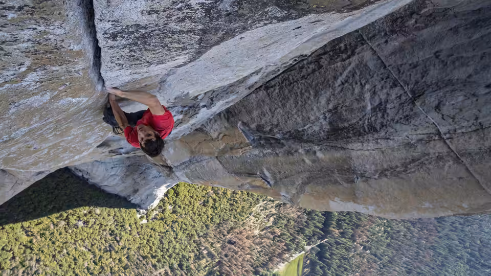 Alex Honnold free soloing a sheer granite wall high above a valley