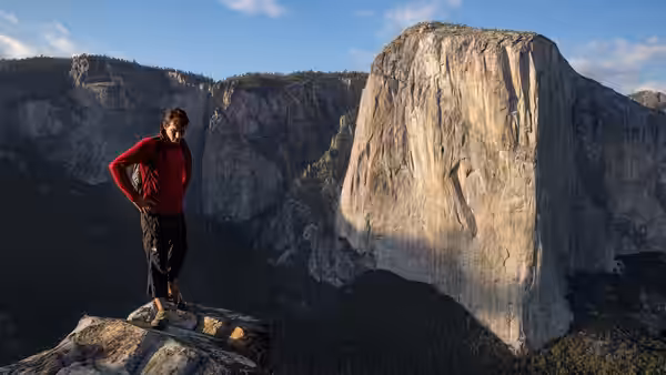 Alex Honnold standing on a rocky ledge with El Capitan behind him