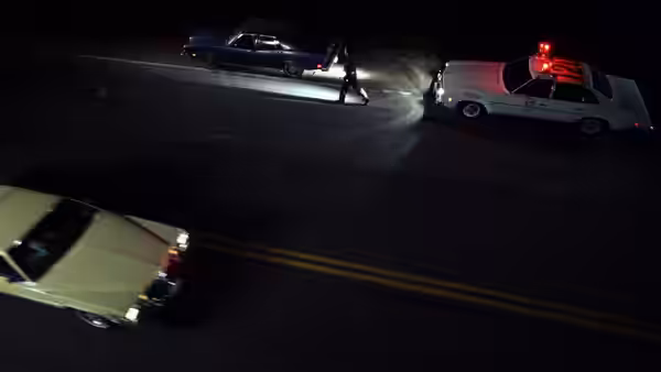 Police officer shines flashlight at a blue car beside a patrol vehicle at night