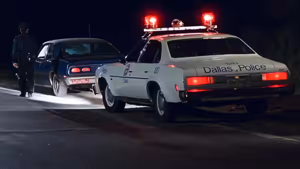 Dallas police car with lights on parked near a blue sedan at night