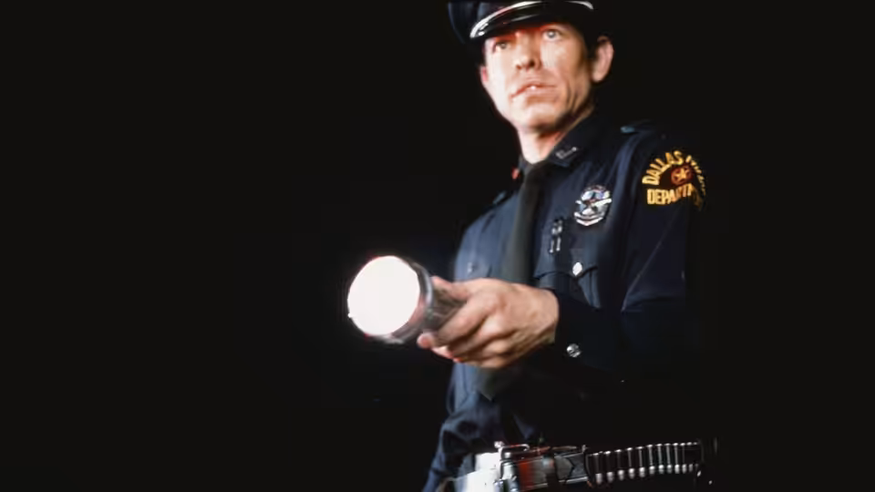 Dallas police officer holds a lit flashlight against a dark background