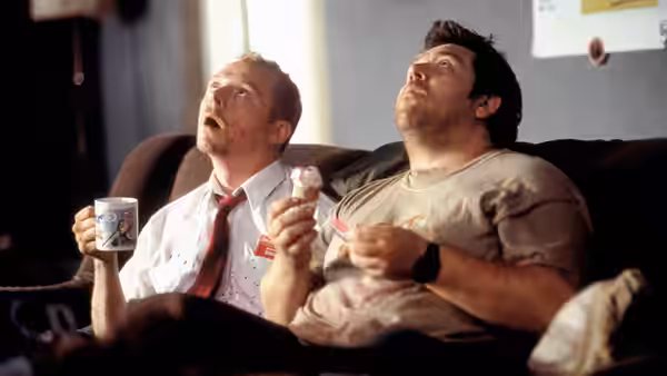 Shaun (Simon Pegg) and Ed (Nick Frost) lounging on a sofa holding snacks