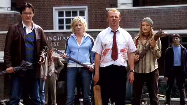 Shaun (Simon Pegg) and companions standing armed outside a brick building