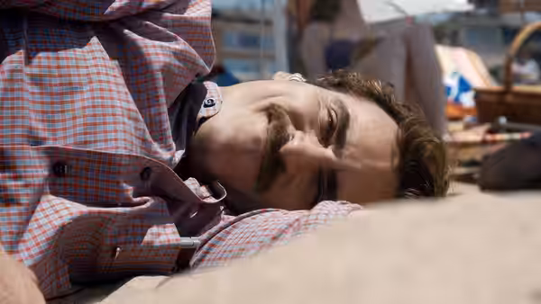 Theodore (Joaquin Phoenix) lies on the sand at the beach in a checkered shirt