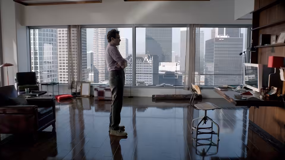 Theodore (Joaquin Phoenix) stands with arms crossed in an empty high-rise office overlooking the city