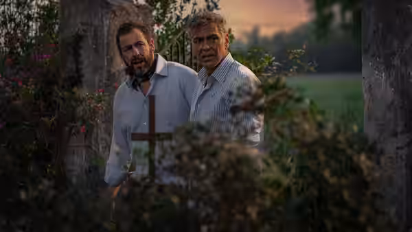 Ron Sukenick (Adam Sandler) and Jay Kelly (George Clooney) standing near a wooden cross outdoors