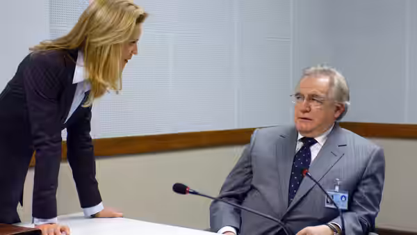 A blonde woman in a suit leaning over a seated older man