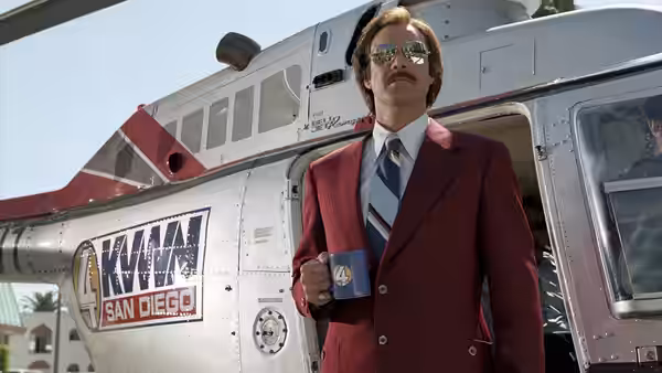 Ron Burgundy (Will Ferrell) standing by a helicopter holding a coffee mug